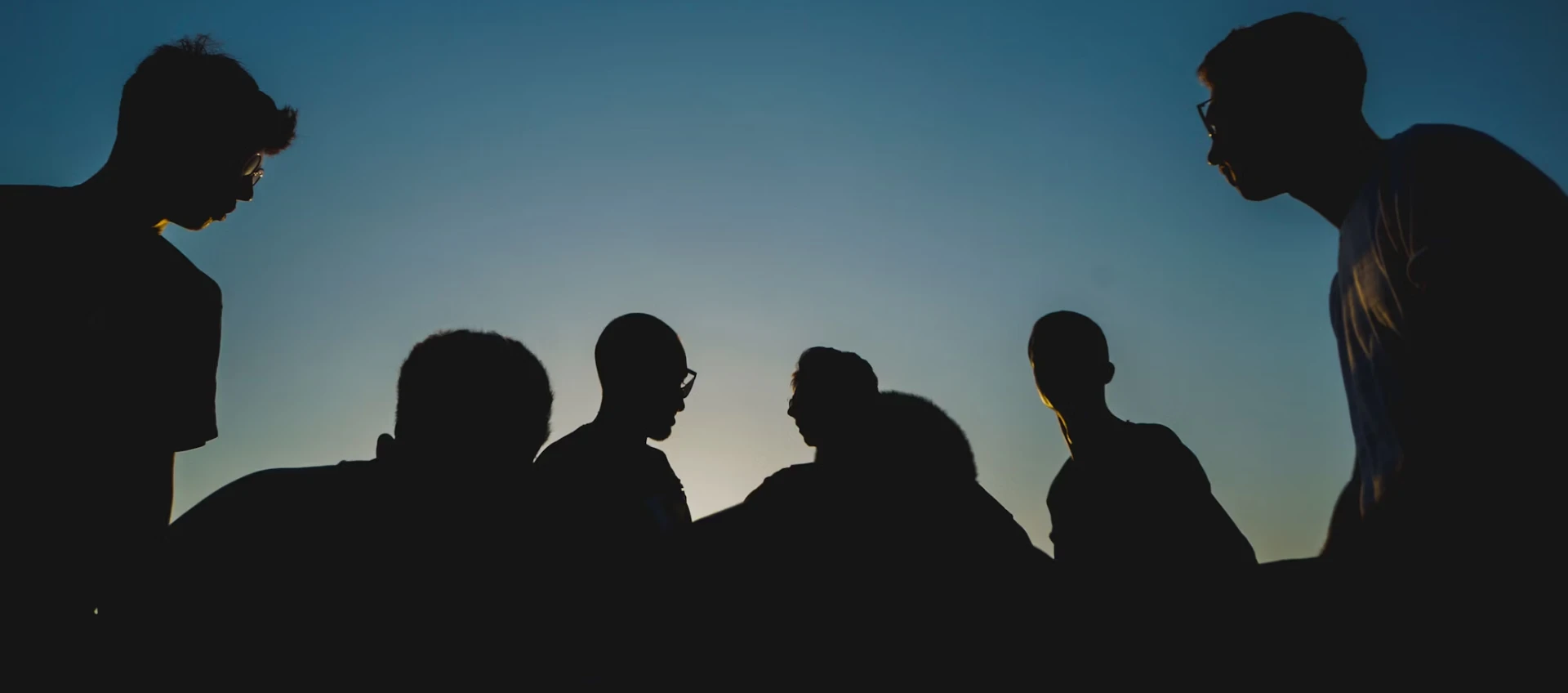 Silhouettes of six people from the Youth Initiative gathered and interacting against a dusk sky backdrop.